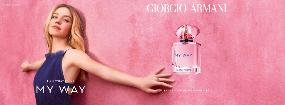 Werbung für Giorgio Armani My Way Eau de Parfum Nectar. Links im Bild steht eine junge Frau mit langem blondem Haar und einem dunklen, ärmellosen Kleid vor einer rosa Wand. Sie streckt beide Arme zur Seite aus und blickt entspannt nach vorn. Daneben steht in weißer Schrift: 'I am what I live – My Way'. Rechts ist eine rosa Parfumflasche mit blauer Kappe und der Aufschrift 'My Way – Giorgio Armani' abgebildet. Oben steht 'Giorgio Armani', unten 'The New Eau de Parfum Nectar'. Oben links ist klein der Name 'Sydney Sweeney' zu lesen.