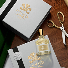 Creed Aventus for Her Parfum mit Geschenkbox und goldener Schere auf Holztisch