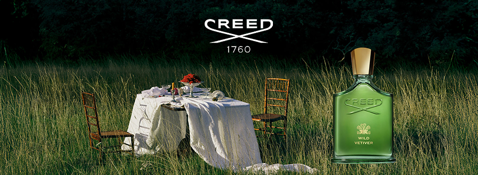 Creed Wild Vetiver Duftflakon vor einer Wiese mit gedecktem Picknicktisch und Stühlen