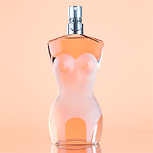 Jean Paul Gaultier Classique Eau de Toilette in einem Flakon in Form eines weiblichen Torsos mit transparentem Glas und rosa Farbverlauf, vor einem zarten Pfirsich-Hintergrund.