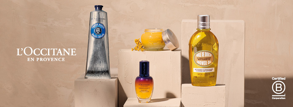 L'Occitane en Provence Produkte auf beigefarbenen Podesten, darunter eine silberne Handcreme, ein gelber Tiegel, ein blau-gelbes Serumfläschchen und eine gelbe Duschölflasche. Rechts unten das Certified B Corporation Logo.