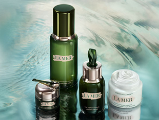 Kategoriebild von La Mer: Mehrere grüne und weiße Pflegeprodukte der Marke La Mer stehen auf einer glänzenden Wasseroberfläche. Zu sehen sind Cremetiegel und Flakons mit silbernen Verschlüssen vor aquatisch schimmerndem Hintergrund.