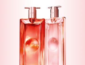 Lancôme Idôle Duftflakons in korall- und rosafarbenem Design mit Pumpaufsatz vor hellem Hintergrund.